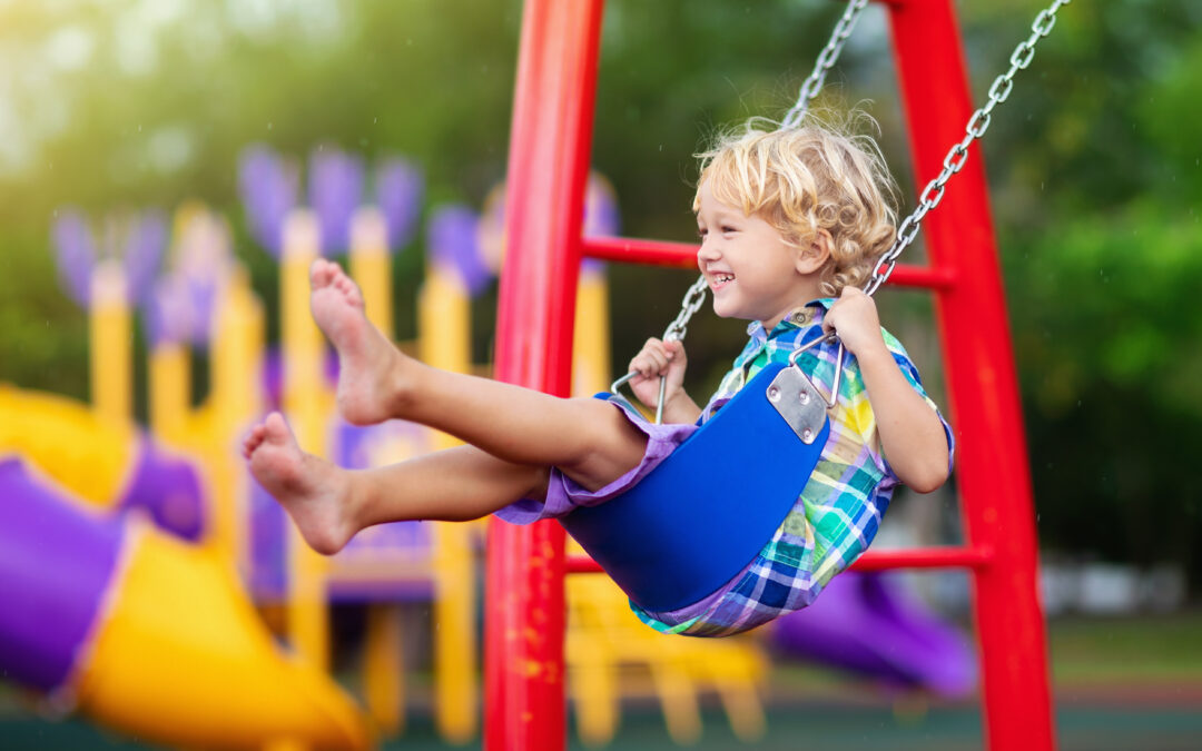 Young blond boy swinging on swing set at public playground